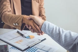 Two people shaking hands over a pile of papers