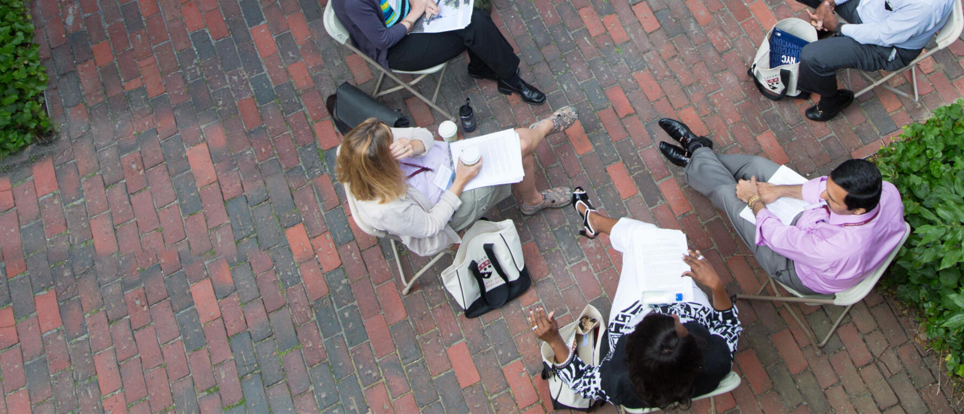 A group of academics sit in a circle collaborating in a courtyard. 